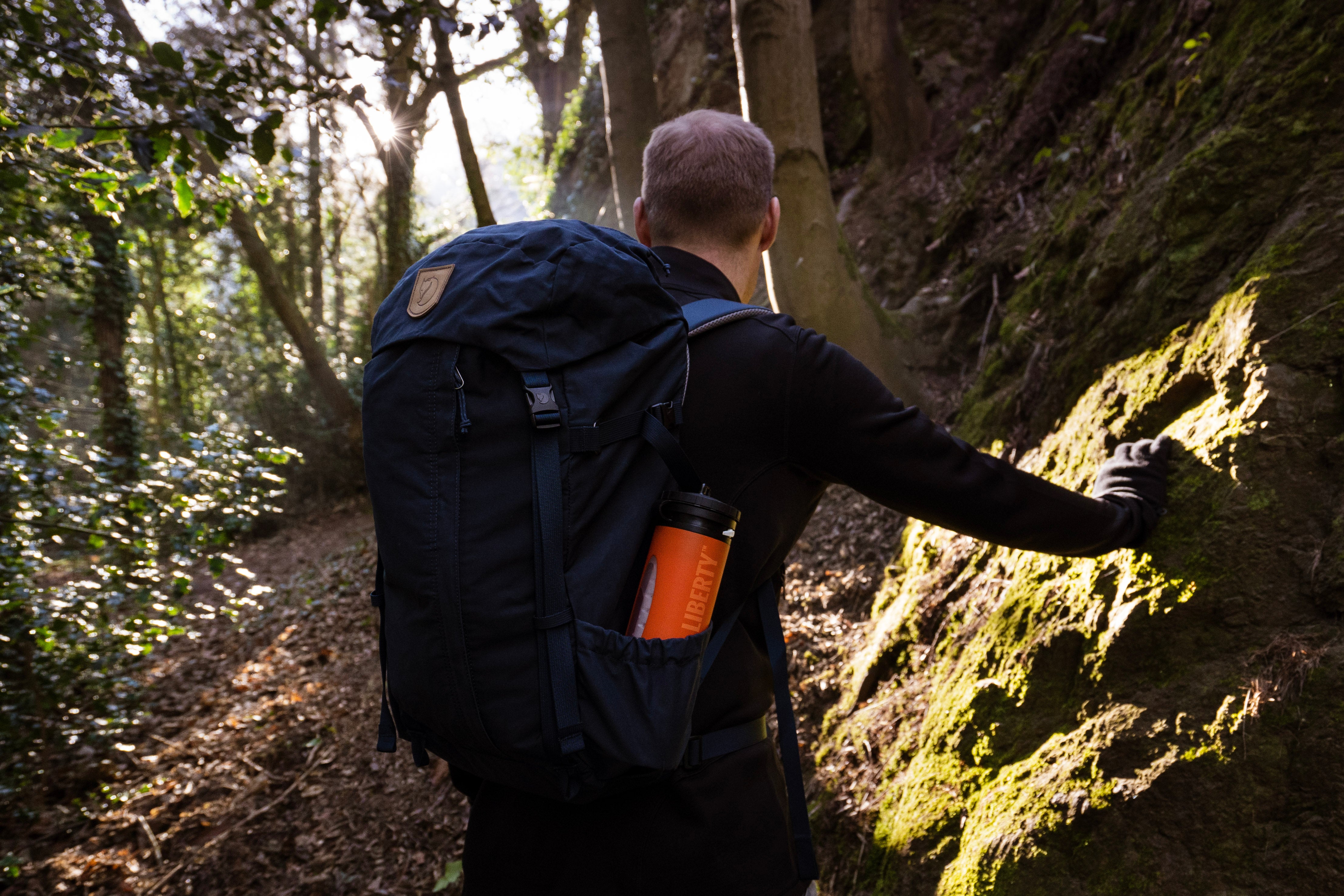 Hiker climbing a steep forest path with an orange LifeSaver Liberty in his backpack