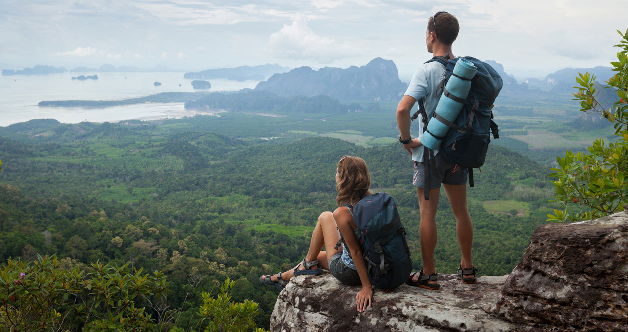 Two hikers with backpacks overlooking a scenic landscape with mountains and water.