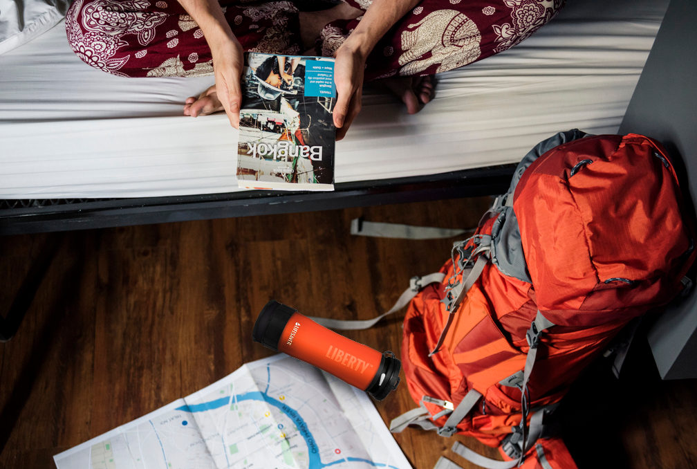 Person holding a book titled 'Bangkok' next to an orange backpack and map on a wooden floor.