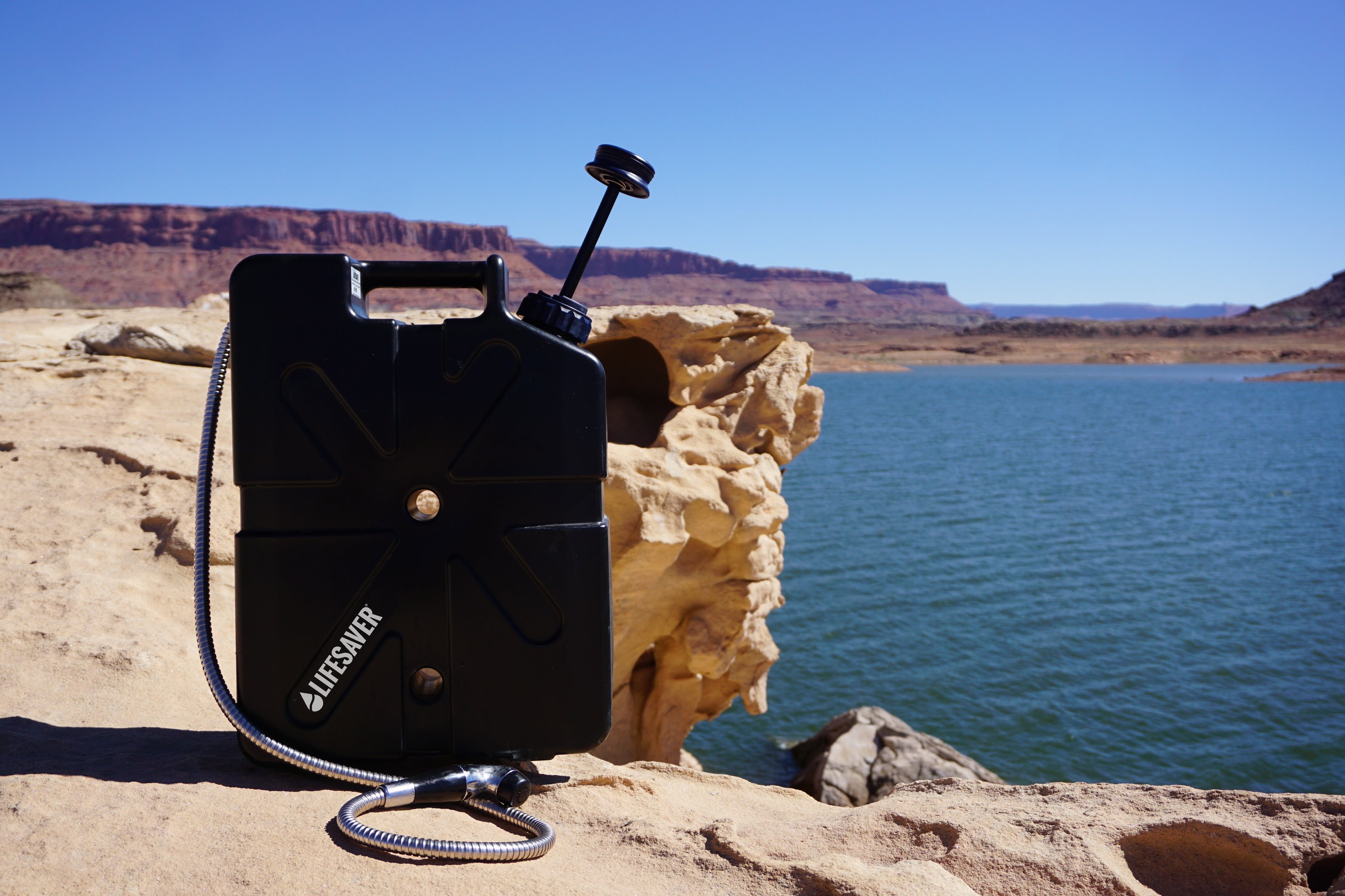 Black LifeSaver Jerrycan with a shower attachment attached on a rocky cliff overlooking a body of water.