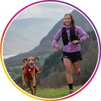 Woman running with a dog on a trail with mountains in the background