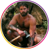 Man with a beard holding an axe, sitting on the ground with a natural background