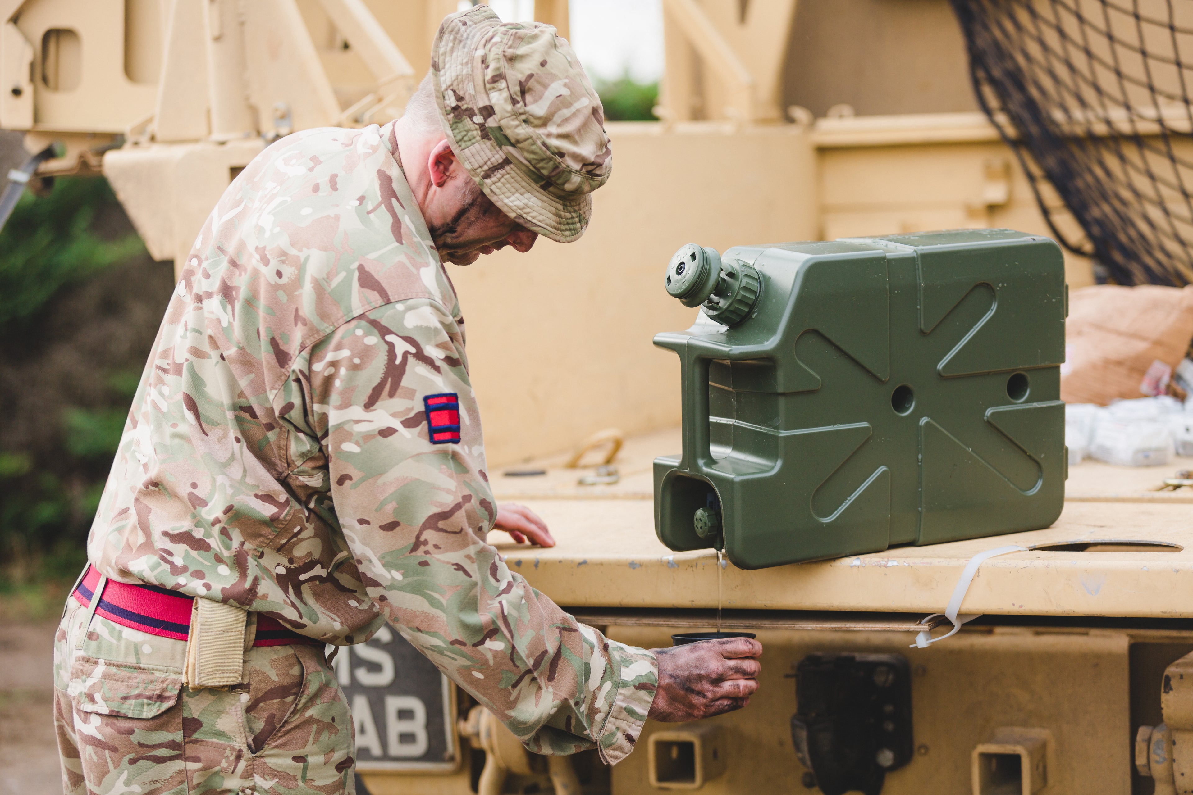 Soldier in camouflage uniform interacting with a green LifeSaver Jerrycan on a military vehicle