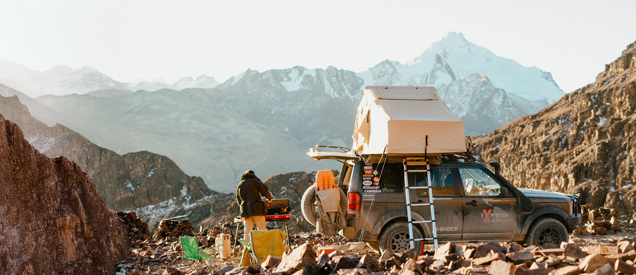 Person camping in a remote mountainous area with a vehicle and rooftop tent.