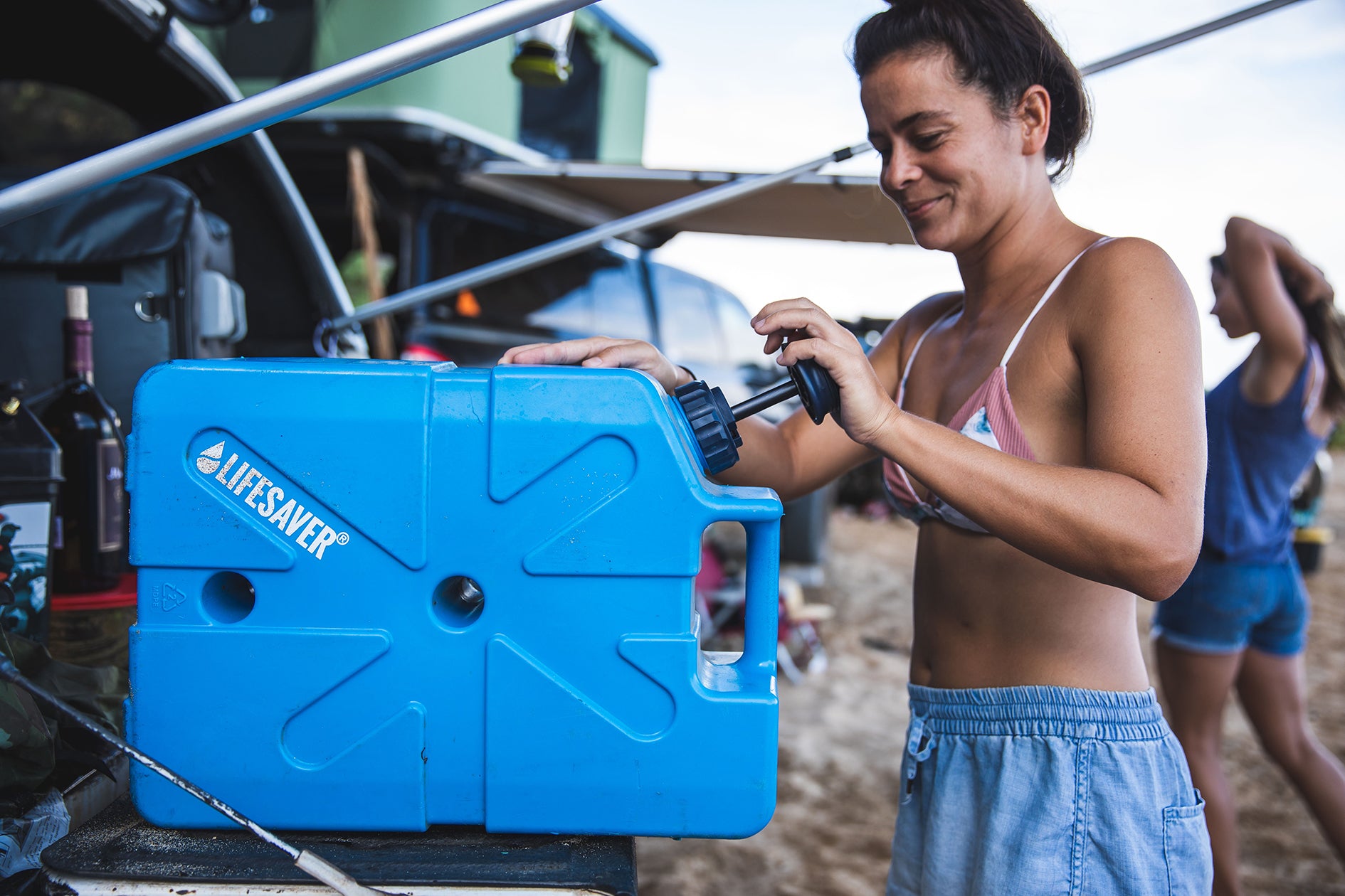 Woman using a blue 'Lifesaver' Jerrycan at an outdoor event.