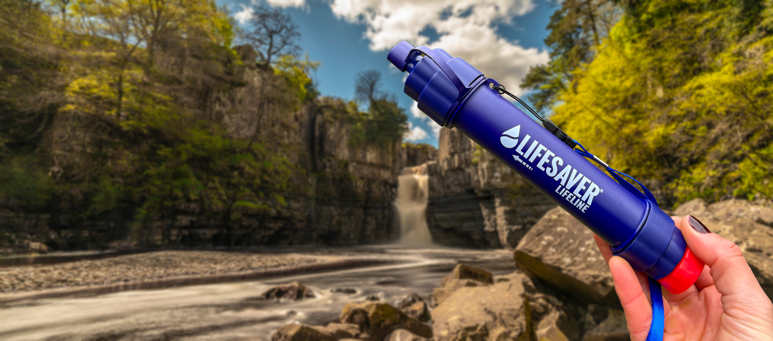 Lifesaver water filter held by a hand with a scenic background of a waterfall and rocks.