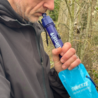 Person using a LifeStraw water filter in a natural setting
