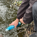 Person holding a blue water bottle over a body of water