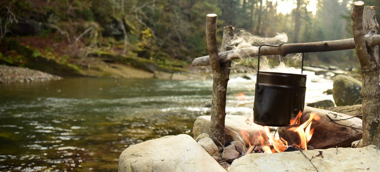 Black pot over a campfire by a river with trees in the background